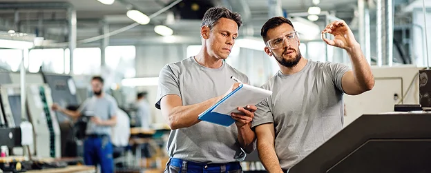 Deux ouvriers inspectent une pièce de fabrication en usine.