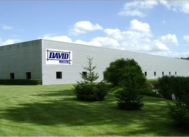 Bâtiment industriel gris avec le logo DAVID INDUSTRIES, pelouse verte et ciel bleu.